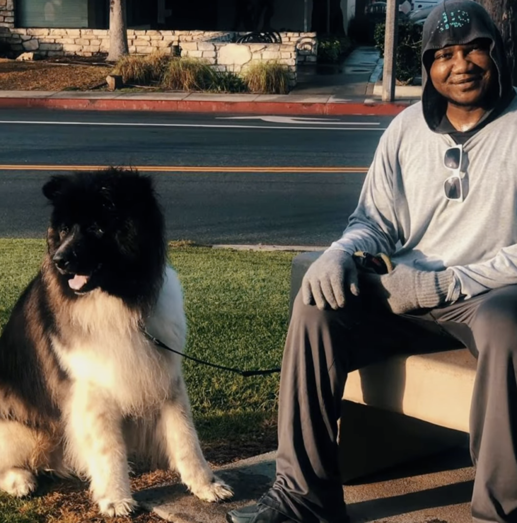 Dr. Sanusi Umar seated outdoors beside a large black and white dog.