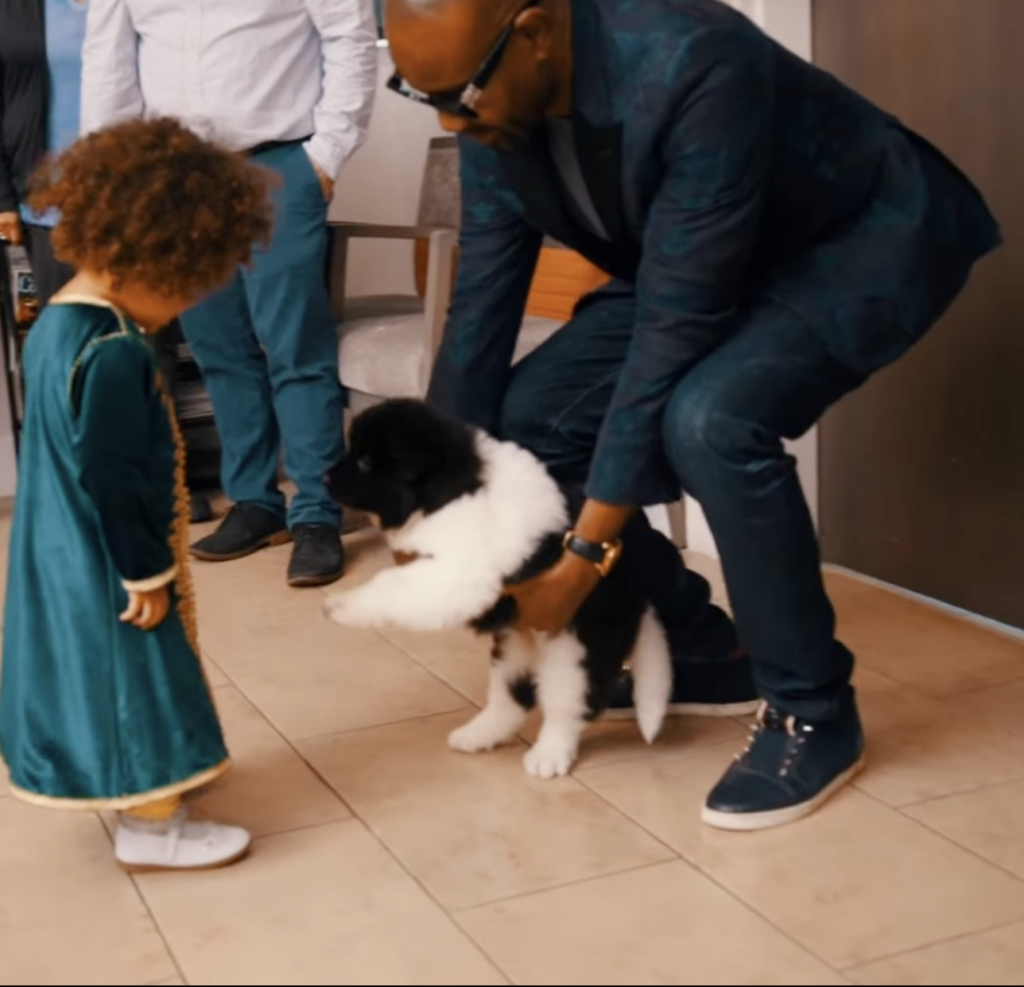 Dr. Sanusi Umar holding a black and white puppy near a young child indoors.