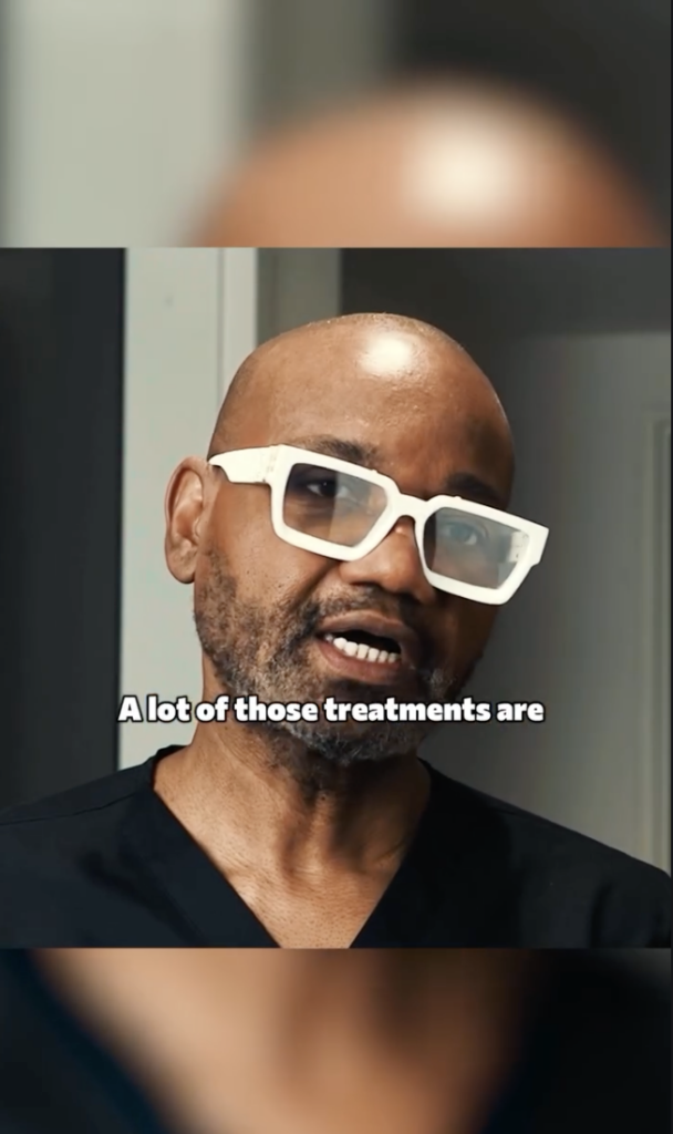 Dr. Sanusi Umar wearing white glasses and black scrubs while speaking indoors.