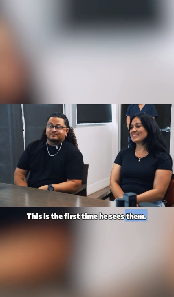 Juan and his wife seated together in a clinic room, both looking forward and smiling.