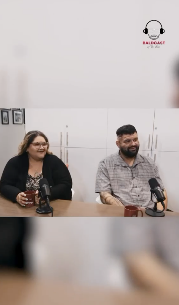 Man and woman seated beside each other at a table with microphones and red mugs.