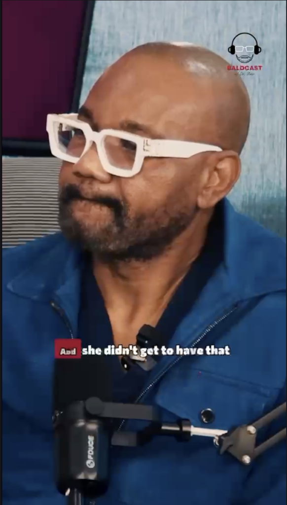 Dr. Sanusi Umar wearing white glasses and a blue jacket while seated at a podcast microphone.